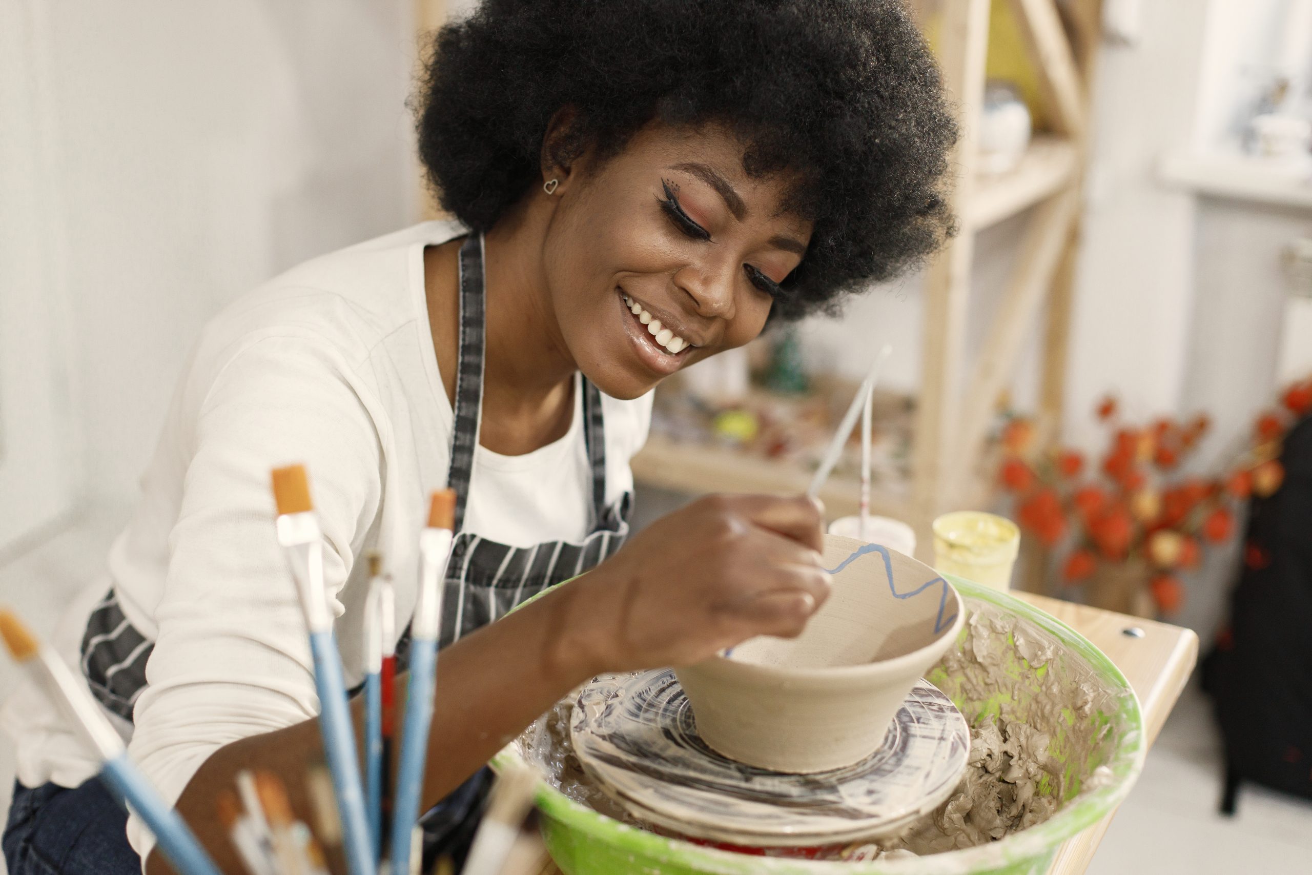 young black woman painting clay pot art studio craftswoman painting ceramic bowl workbench girl wearing blue apron scaled